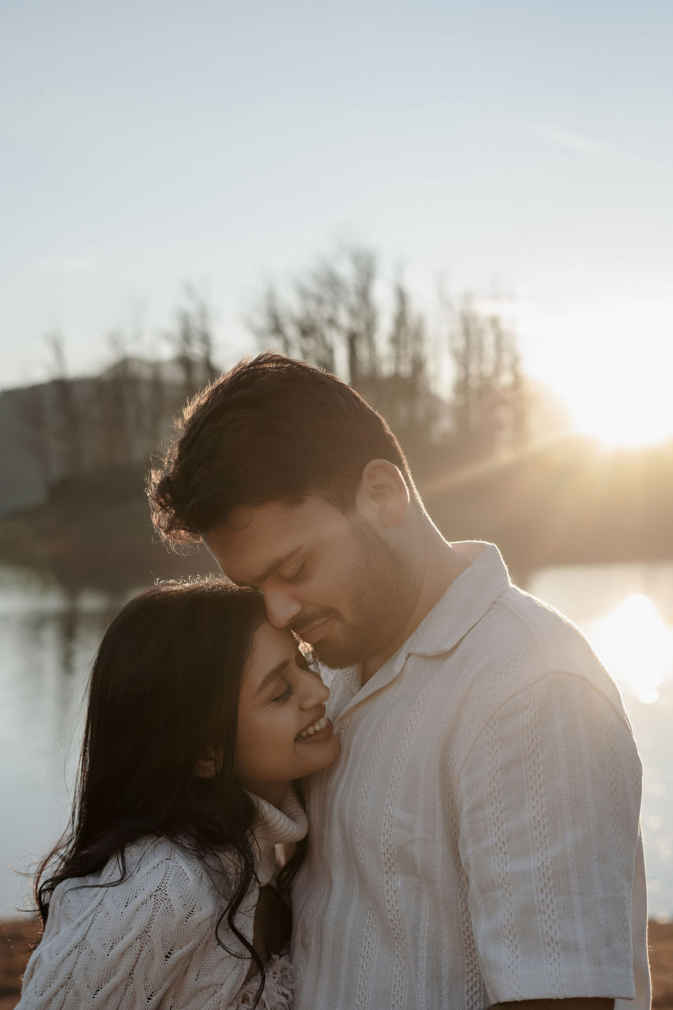 Couple embracing by a lake at sunset.