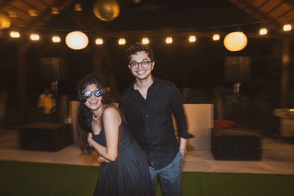 Two people smiling under string lights at night.