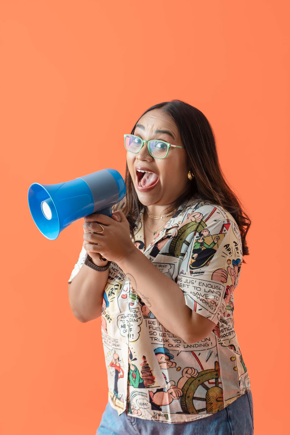 Soumya Venugopal excitedly holding a blue megaphone, orange background.