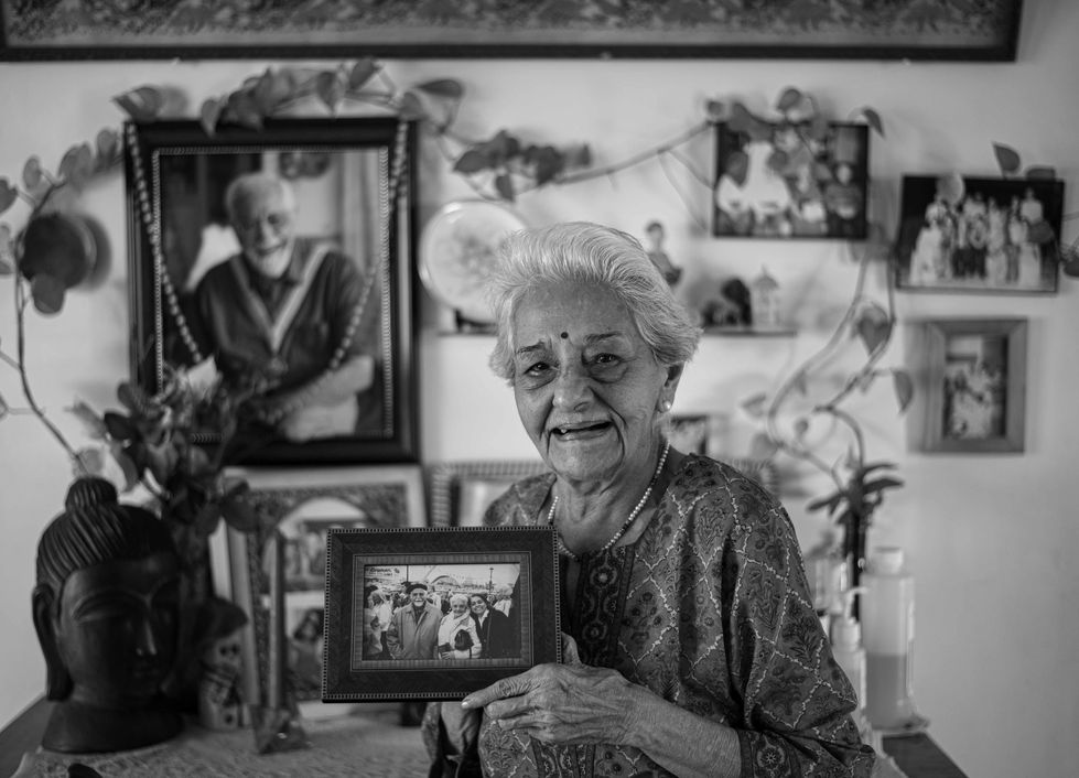 Elderly woman holding a framed photograph, smiling warmly.