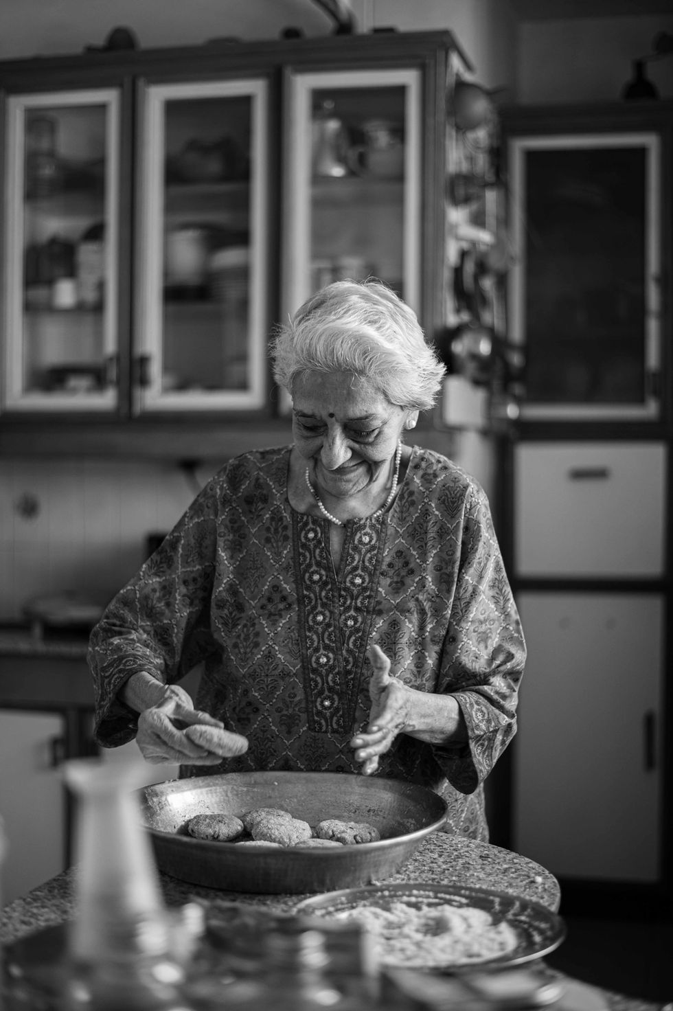 Elderly woman cooking in a kitchen, black and white.