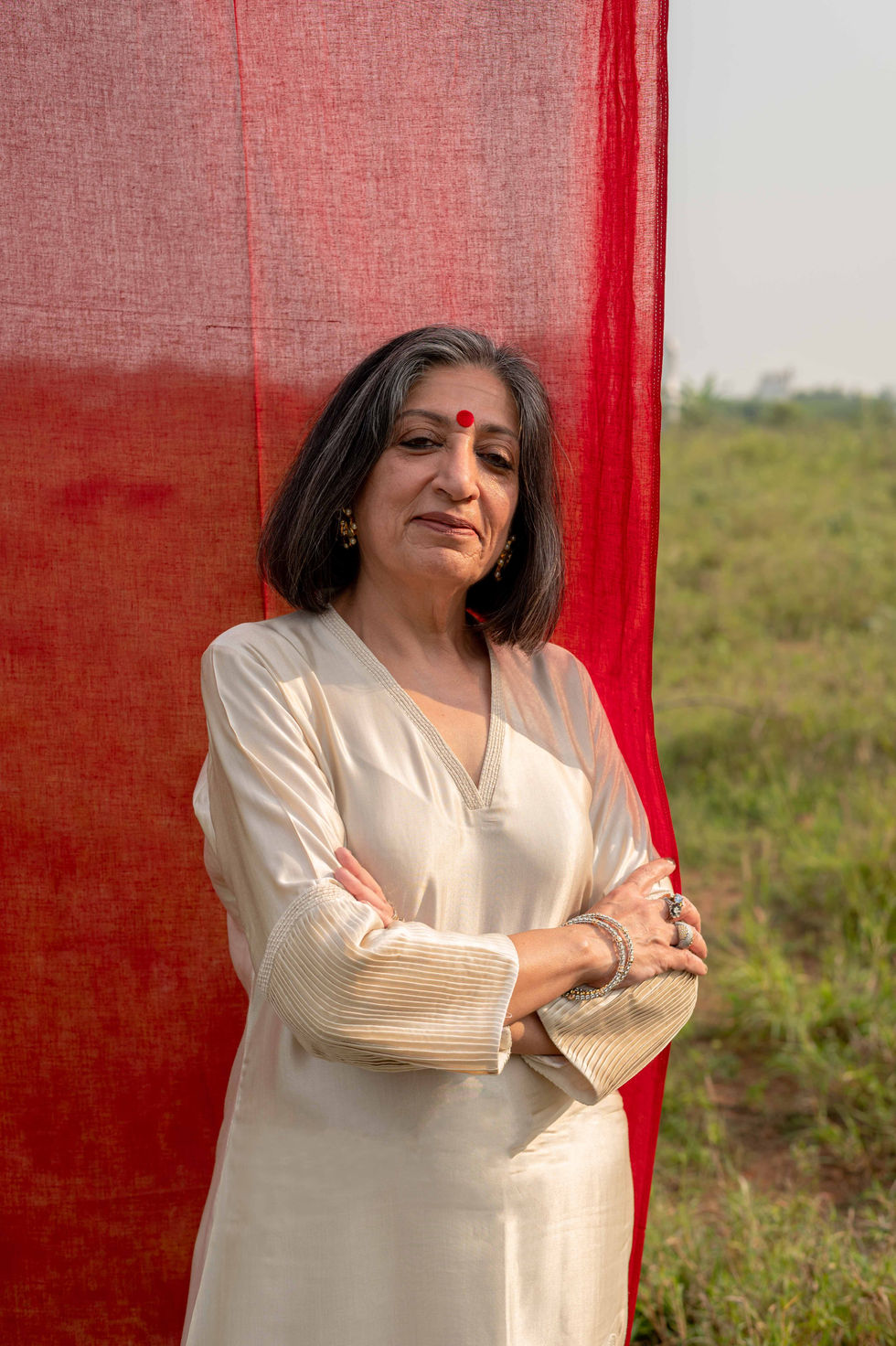 Woman standing with arms crossed, red background curtain.