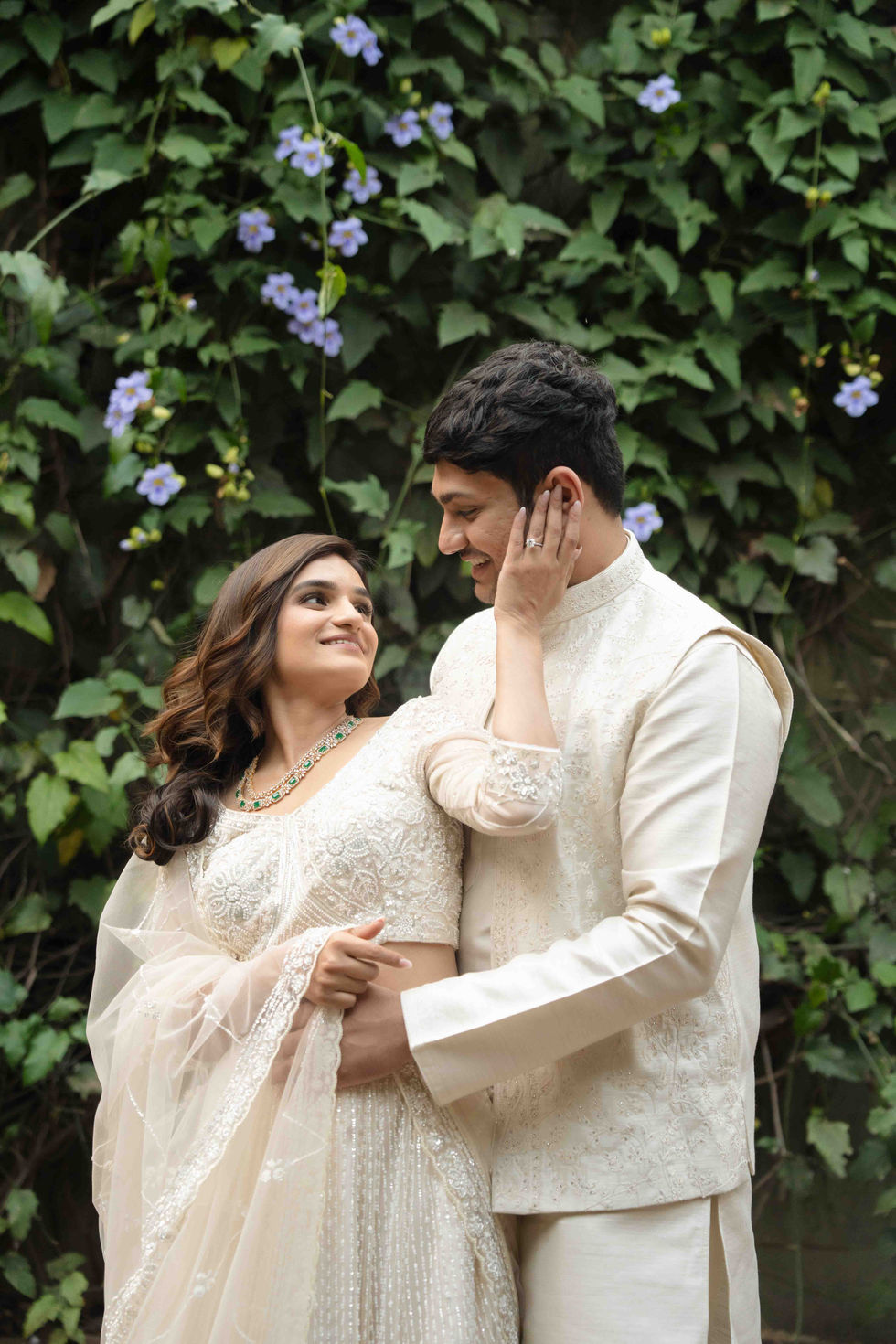 Bride and groom embracing in front of leafy, floral background.