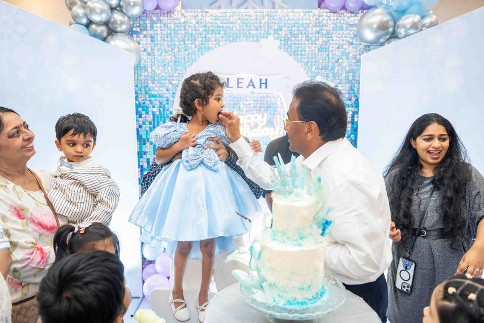 Child in blue dress at birthday party with cake.