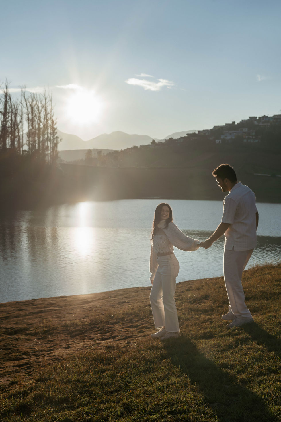 Couple holding hands by a serene lakeside at sunset.