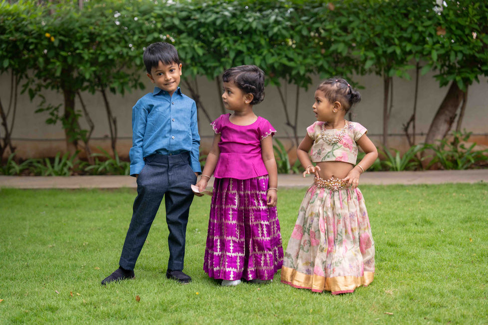 Three children in colorful traditional outfits outdoors.