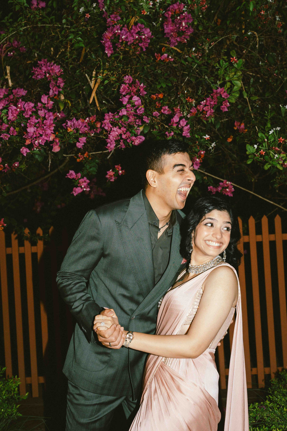 Couple laughing, surrounded by vibrant flowers at night.