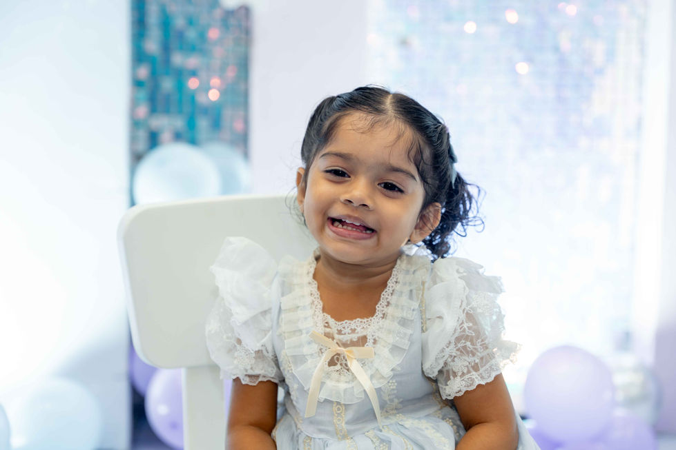 Smiling child in a white dress with balloons.