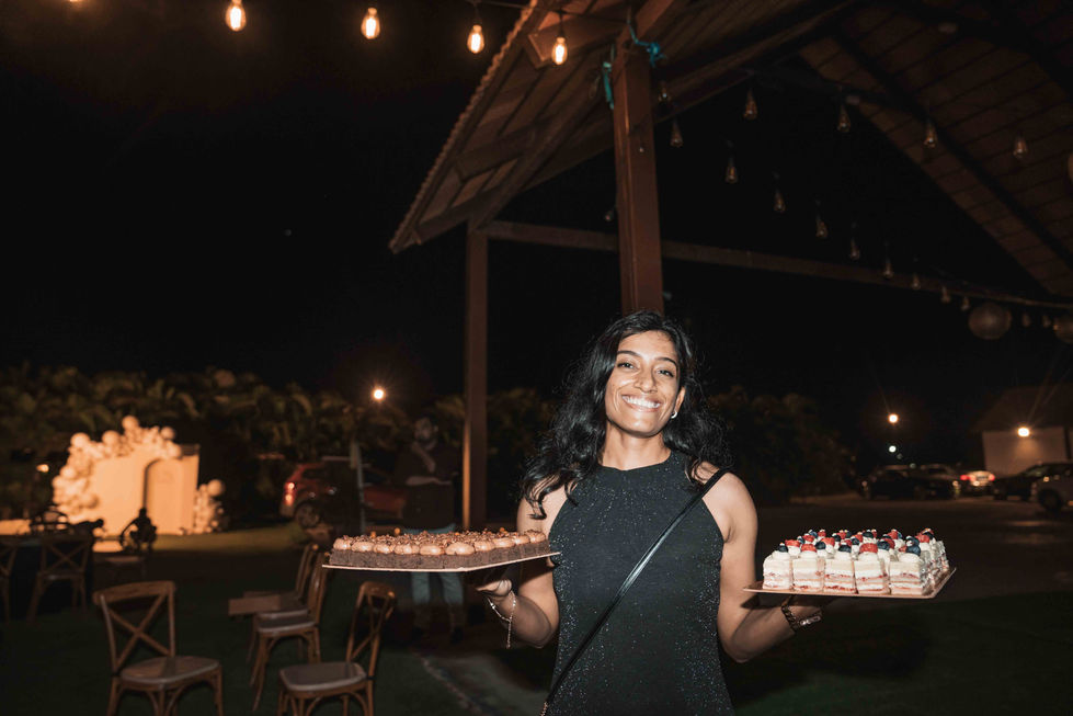 Smiling person holding trays of desserts at night.