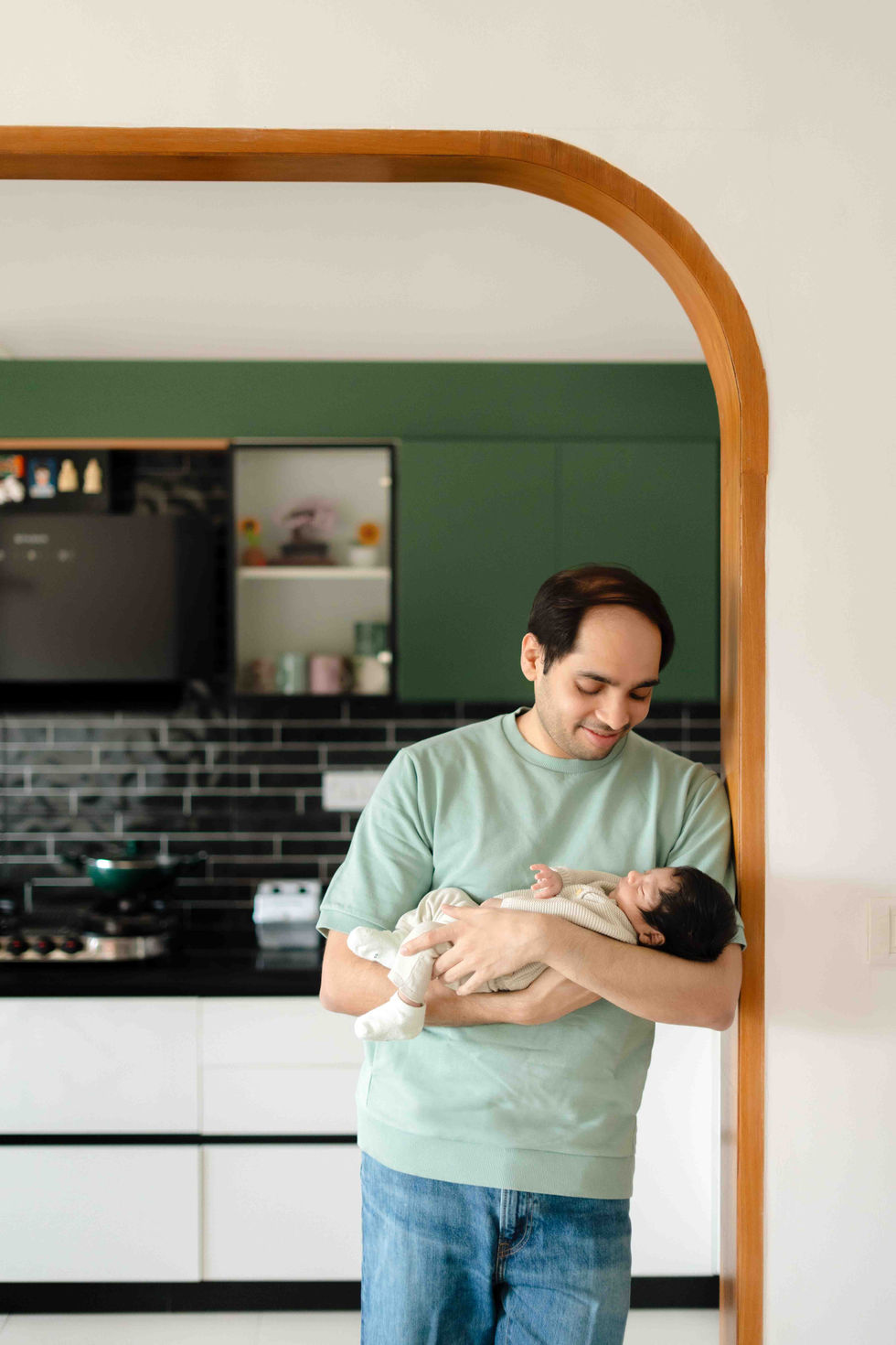 Man holding newborn baby in a modern kitchen setting.