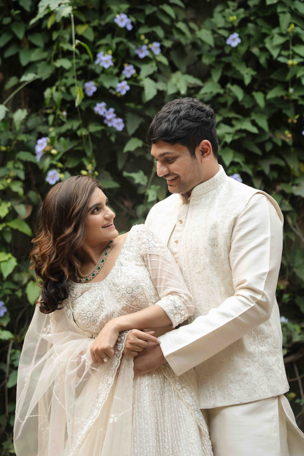 Bride and groom in traditional attire, smiling in a garden.