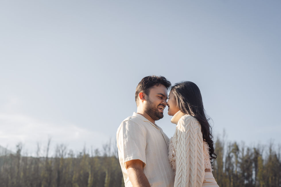 A couple smiling, embracing outdoors under clear sky.