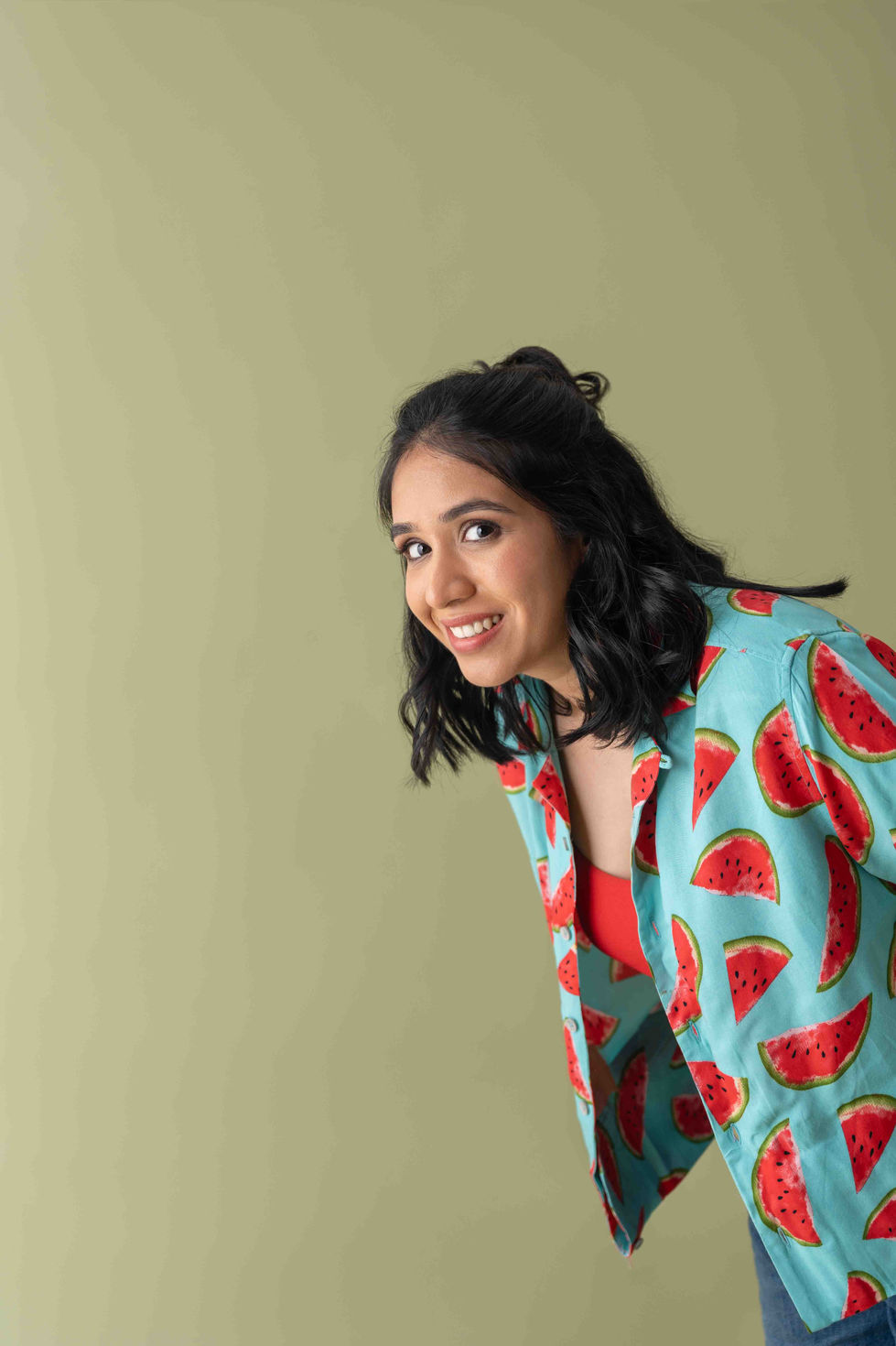 Smiling Ramya Ramapriya in watermelon-patterned outfit, green background.