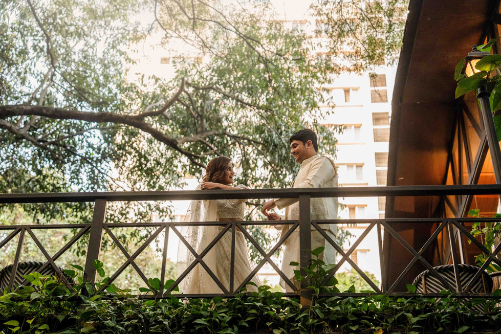 Bride and groom standing on a bridge surrounded by greenery.