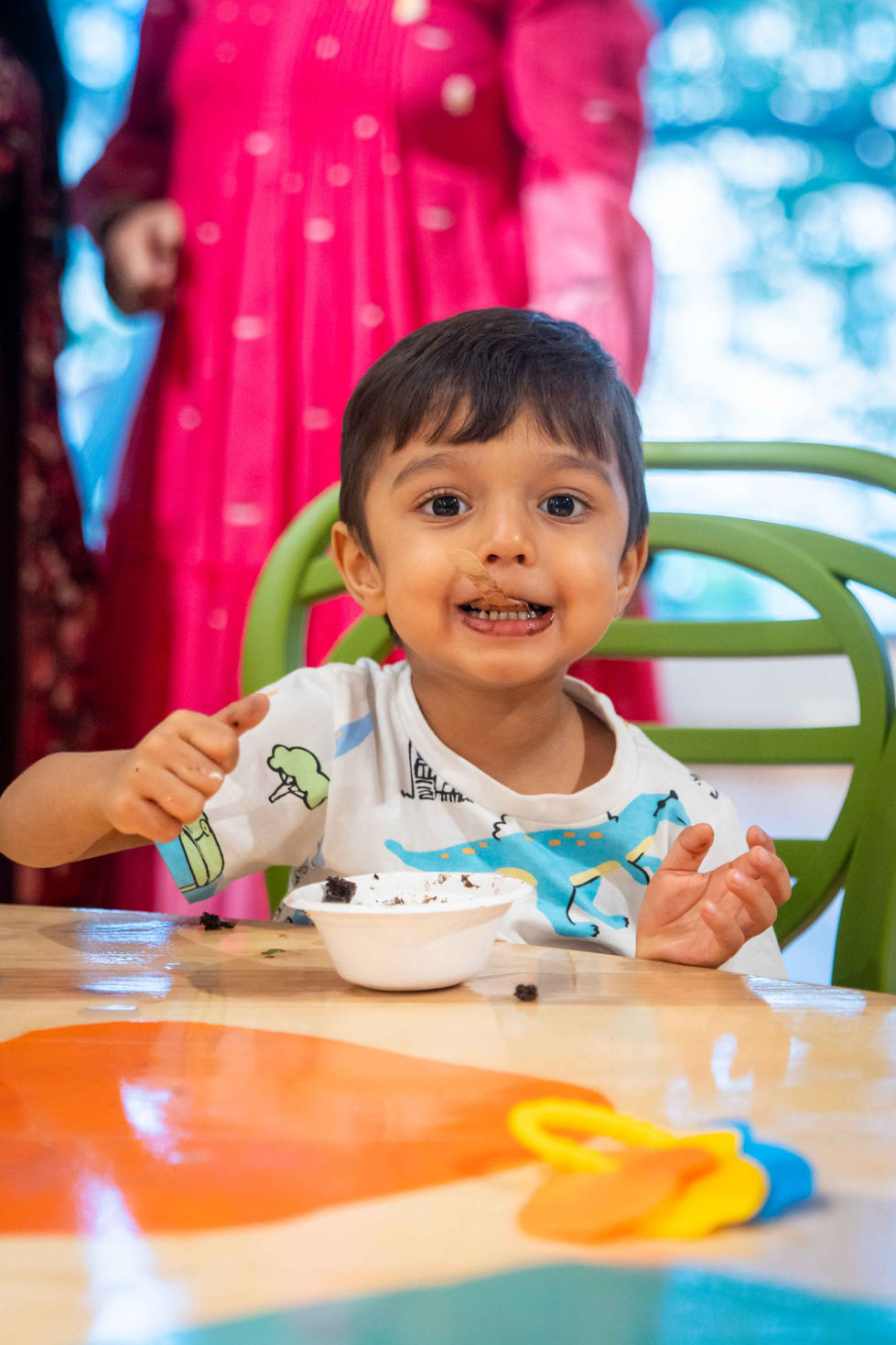Child eating dessert at a table, smiling happily.