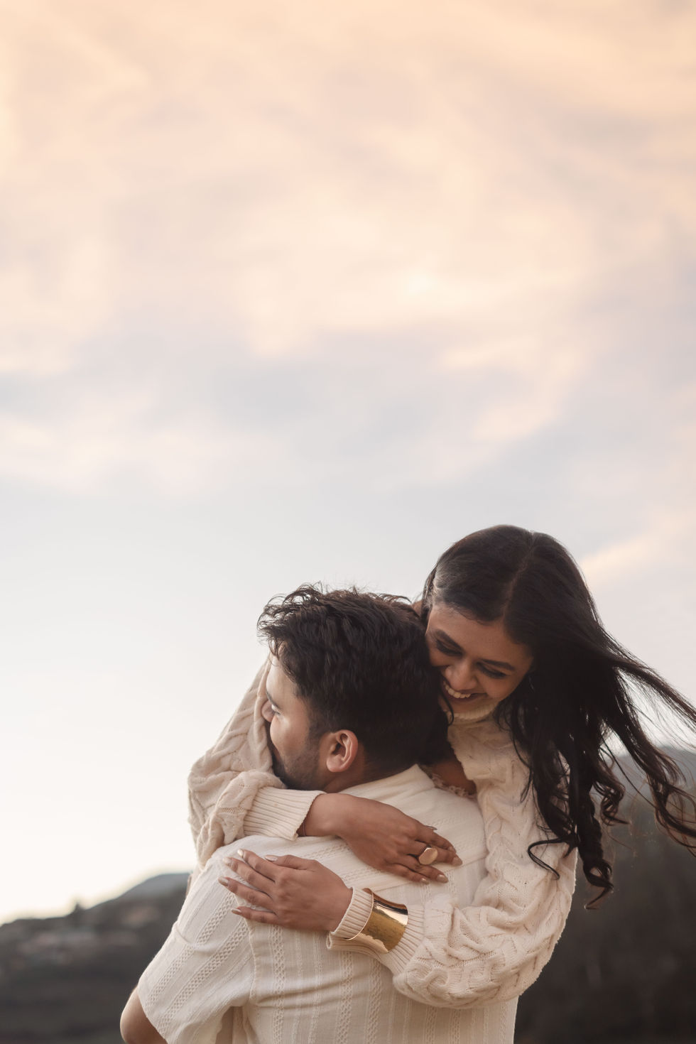 Couple embracing under a soft, cloudy sky.