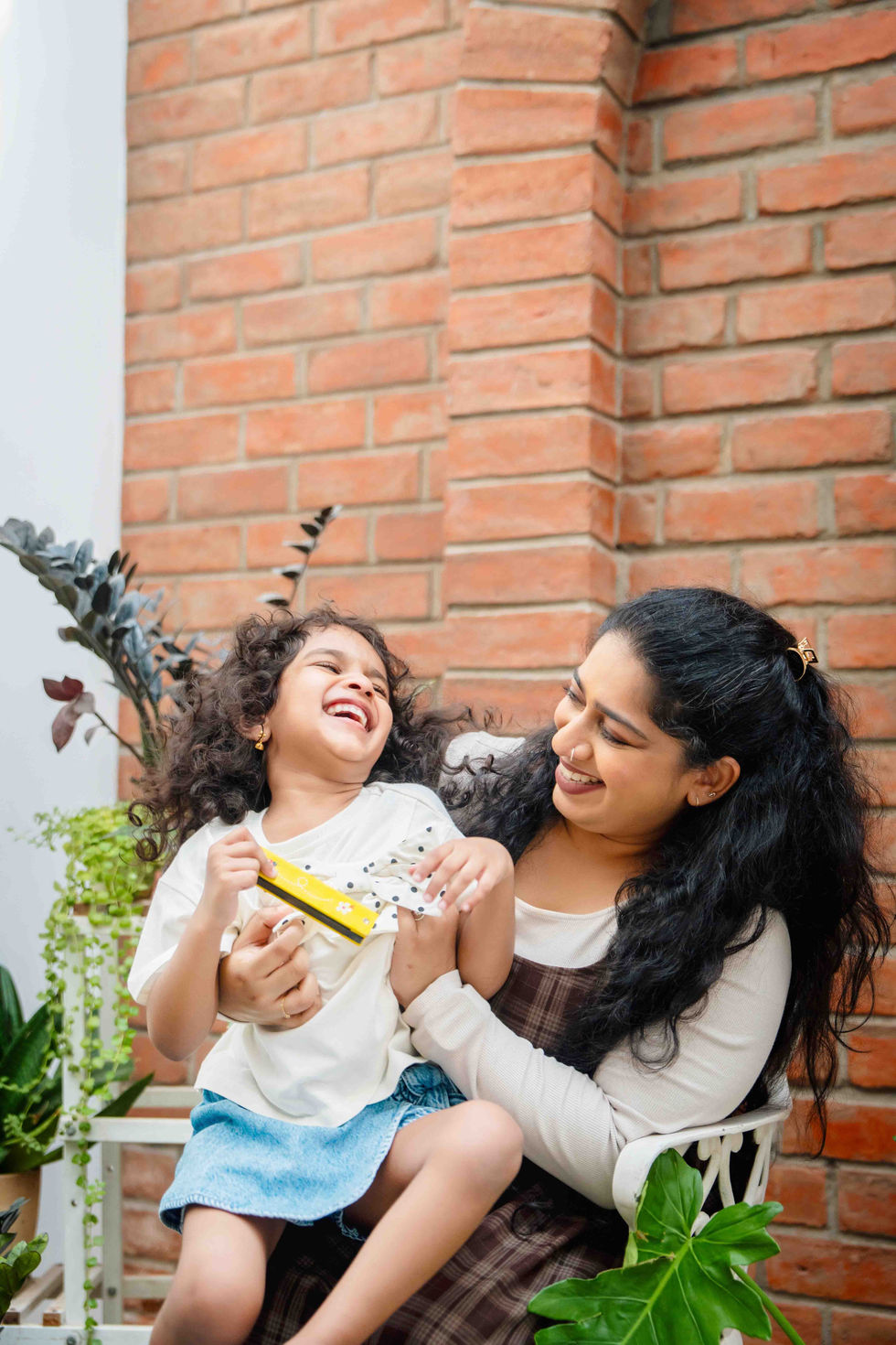 Woman and child laughing together near brick wall.
