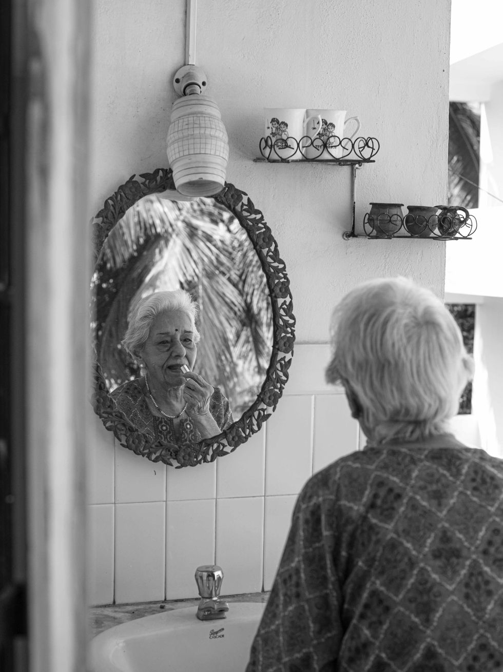 Elderly person looking in mirror, applying lipstick.