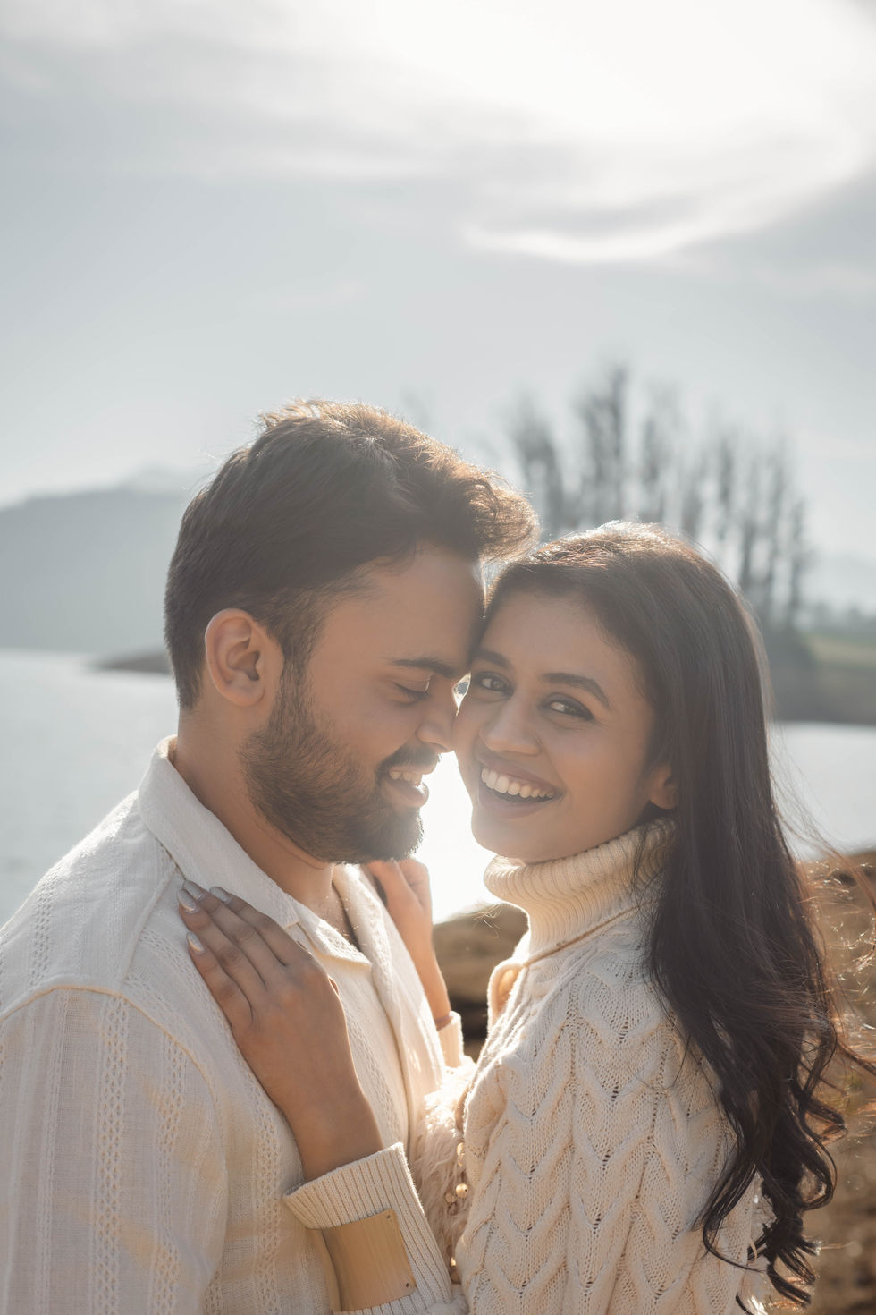 Couple embracing near a serene lake backdrop.