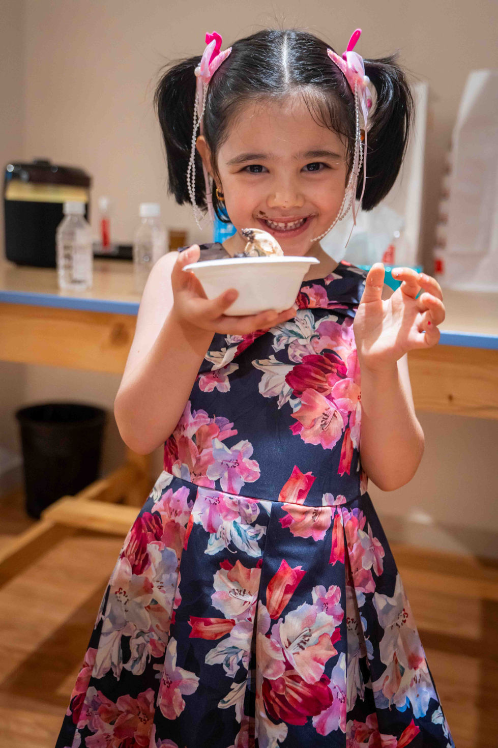Smiling child holding a bowl, wearing floral dress.