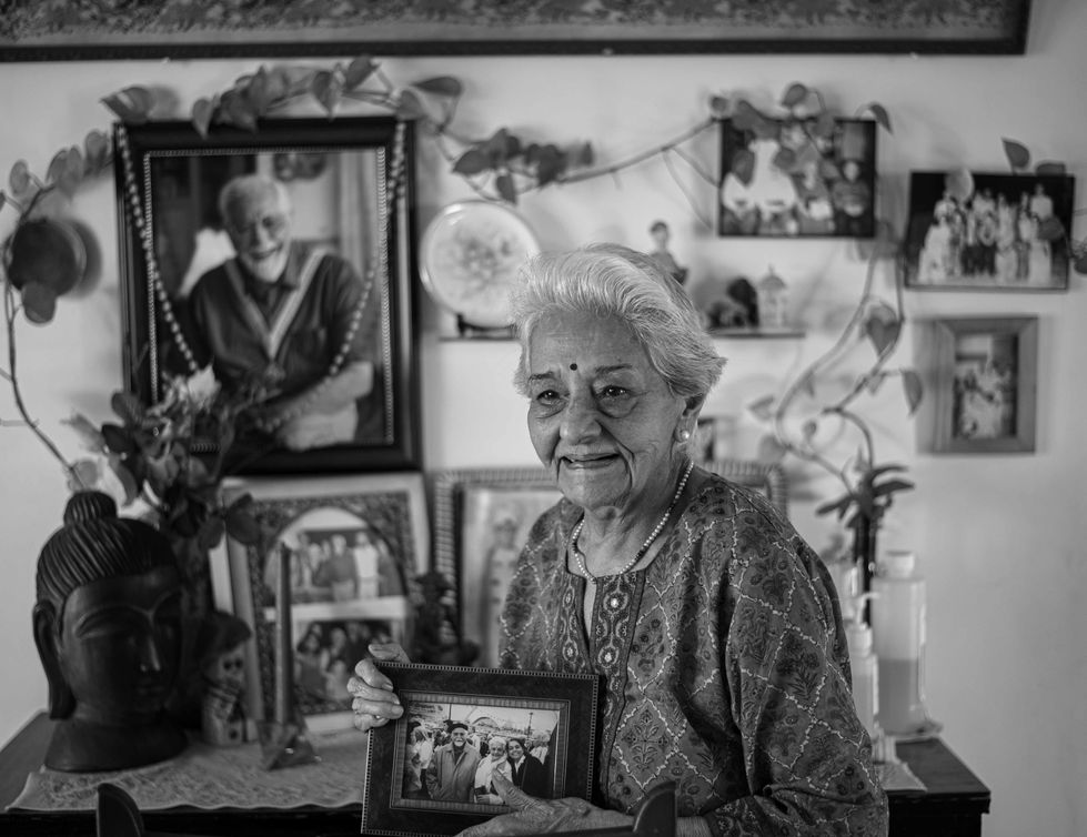 Elderly woman holding a framed photograph, surrounded by portraits.