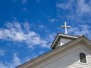 Wooden cross on a simple steeple set against a sunny summer blue sky.