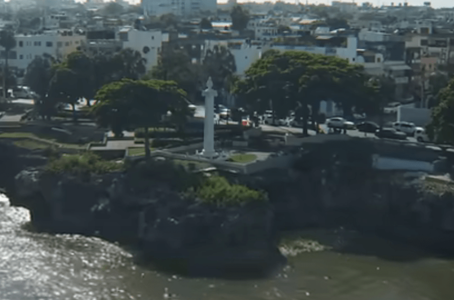 Mientras paseas por el Malecón de Santo Domingo, una columna inofensiva podría llamar tu atención, erigiéndose como un guardián silencioso del puerto. Quizás nunca le prestaste atención ni pensaste en su significado. Sin embargo, esta estructura discreta es un recordatorio sombrío de muchas vidas perdidas, ligadas a la aterradora historia de la desembocadura del río Ozama. ¿Qué oscuros secretos se esconden bajo sus cimientos? ¿Por qué hubo tantos encuentros trágicos en esta zona? ¿Cómo ha marcado esta columna el legado de la ciudad? Esta es la historia de la columna de la Aurora, que ha dejado una huella horrorífica en la historia del puerto de Santo Domingo. La Columna de la Aurora: Un Recordatorio de Vidas Perdidas en la Desembocadura del Río Osama El malecón de Santo Domingo es un lugar donde la historia y la naturaleza se entrelazan en un drama que ha marcado la ciudad. Una columna inofensiva, pero silenciosa, puede llamar la atención del paseante, recordándole la sombría historia de la desembocadura del río Osama. Esta estructura discreta es un recordatorio de las vidas perdidas en la zona, donde la combinación de aguas poco profundas y la exposición directa al mar Caribe ha sido una amenaza constante para los barcos y sus tripulantes. La historia de la columna de la Aurora comienza en 1498, cuando Bartolomé Colón fundó Santo Domingo en la margen oriental del río Osama. El puerto se convirtió rápidamente en el principal asentamiento europeo en la isla gracias a su excelente río, que sirvió de puerto. Sin embargo, la desembocadura del río tenía un problema: era extremadamente peligrosa. La plataforma continental era estrecha, lo que permitía que las olas viajaran sin mucha obstrucción y se hagan más grandes en las aguas poco profundas. Además, el choque entre el agua del mar y el agua del río en la desembocadura era un peligro mayor. Decenas de barcos sufrieron daños y naufragaron en los tiempos coloniales, especialmente durante las tormentas. El 27 de septiembre de 1908, un día que Santo Domingo nunca olvidaría, la balandra Aurora, un modesto barco de pesca, naufragó en la desembocadura del puerto. Los tres tripulantes luchaban contra las olas que los arrastraban hacia los acantilados. Sus gritos de auxilio se mezclaban con el rugido del océano, mientras los habitantes de Santo Domingo observaban con horror la tragedia. La comunidad se unió rápidamente para debatir cómo salvar a los marineros y finalmente, un plan se formó. Un grupo de valientes hombres, incluyendo al pescador Emeterio Sánchez, se aferraron a una cuerda lanzada al agua con la esperanza de sacar a los naufragos. Sin embargo, una ola masiva se erigió frente a ellos y violentamente golpeó la costa, llevando consigo a ocho desafortunados. Todos los tripulantes de la Aurora murieron en los acantilados. Después del trágico incidente, se erigió un monumento en 1910 para honrar a las víctimas y a los héroes locales que intentaron el rescate. La columna jónica de 1.5 metros de diámetro y 11 metros de altura termina en un vaso griego con arcos y una piña. Fue diseñada por Abelardo Piñeiro y construida por el ingeniero Osvaldo Baes. La columna ha perdurado las décadas, resistiendo el sol, las olas y los cambios políticos. Pocos años después de la construcción del monumento, el USS Memphis, un crucero acorazado de la Marina de los Estados Unidos, invadió el puerto de Santo Domingo sin previo aviso. Una serie de olas gigantescas arrastraron al USS Memphis hacia la costa, donde fue destrozado contra las rocas. Cincuenta y tres marineros estadounidenses perdieron la vida en los acantilados, y más de 200 resultaron heridos. Este trágico evento sumó a las víctimas del naufragio de la Aurora y a las muertes durante la era colonial, lo que significa que miles de personas han muerto en la desembocadura del río Osama a lo largo de las décadas. La construcción del rompeolas se convirtió en una prioridad después del trágico incidente. Los estudios comenzaron en 1927, y se decidió que se necesitarían muchas rocas grandes para construir la estructura. Se propuso construir un ferrocarril de 13 km desde la cantera hasta un muelle especial para transportar las rocas. Sin embargo, en 1929 no había suficiente dinero y la situación política estaba inestable. El huracán San Zenón golpeó Santo Domingo en 1930, destruyendo la mitad de la ciudad y ahogando cientos, quizás miles, de personas. La obra del rompeolas tuvo que avanzar, y Rafael Leonidas Trujillo tomó el poder en 1930, después de la devastación causada por el huracán. El rompeolas fue inaugurado por Trujillo y ha sido crucial para reducir el impacto de las olas grandes. Los barcos ahora están seguros dentro del puerto, y las mejoras han ayudado a aumentar el tráfico marítimo y el desarrollo económico de la región. El puerto se modernizó mucho, incluyendo la creación de instalaciones como el puerto de San Susi, que se convirtió en un punto clave para el comercio y transporte en el Caribe. La columna de la Aurora es un recordatorio de las vidas perdidas en la desembocadura del río Osama. Aunque ha sido olvidado por muchos, el monumento sigue en pie en el malecón de Santo Domingo, mirando hacia el rompeolas que inspiró. Es un testimonio del espíritu humano frente a la adversidad y un recordatorio de la fuerza de la naturaleza que ha moldeado nuestra existencia y nuestras ciudades.