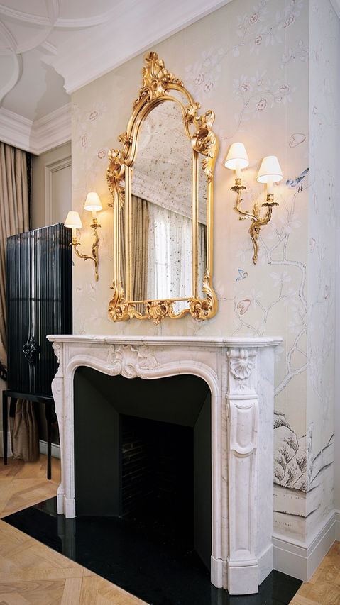 Black fireplace with white rim and a large mirror with gold accents above it