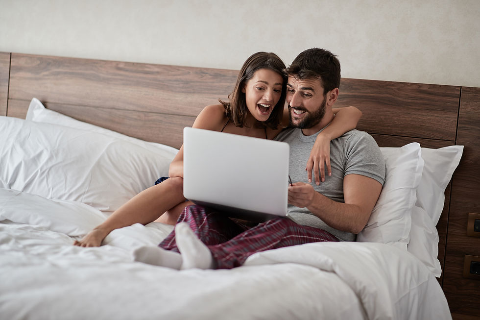 A couple relaxes in bed, engrossed in an exciting show on their laptop, sharing laughter and smiles.