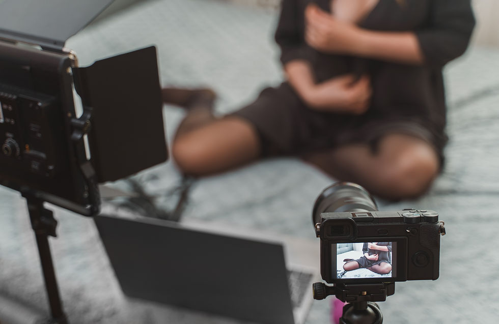 A woman sits on a bed, surrounded by filming equipment, as she prepares to record herself.