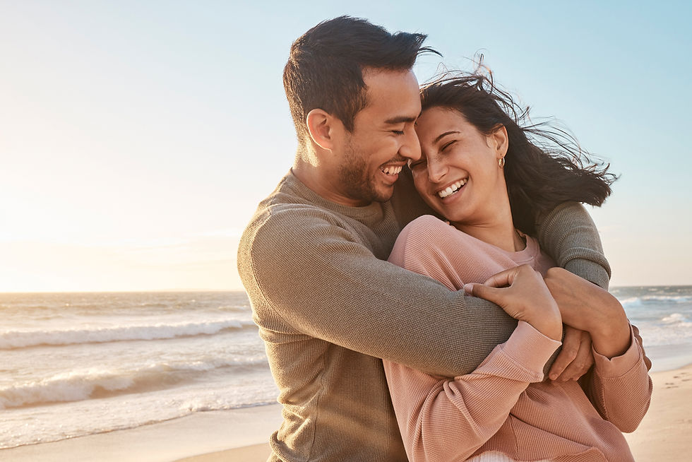 A joyful couple embraces on the beach, their smiles radiating love and happiness as the sun sets behind them.