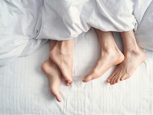 A couples' feet underneath the bed sheets