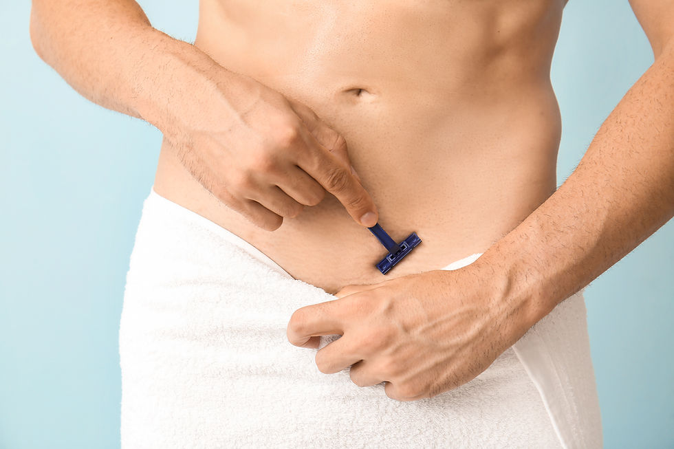 A man carefully shaves his lower abdomen while wrapped in a towel against a light blue background.