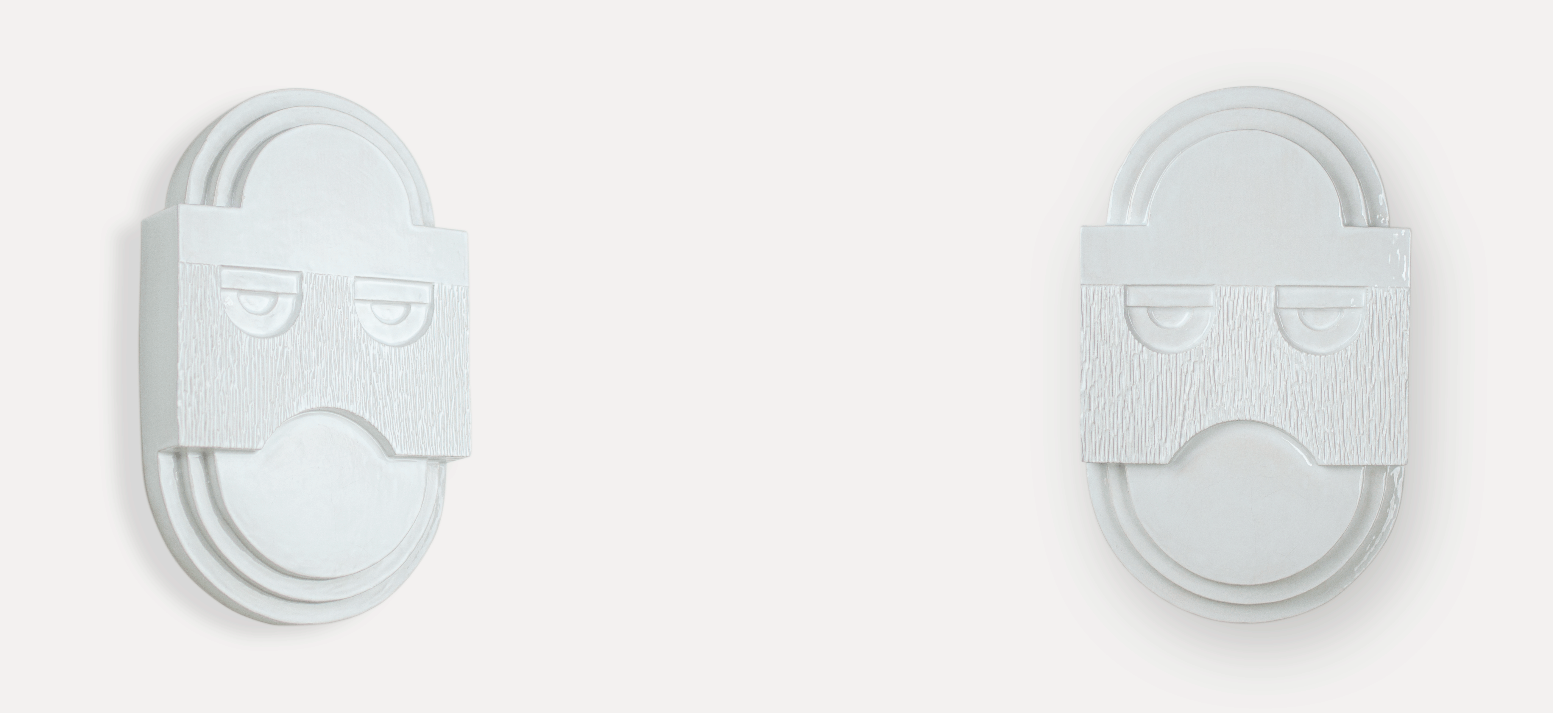 Two white glazed handmade masks hanging an the wall