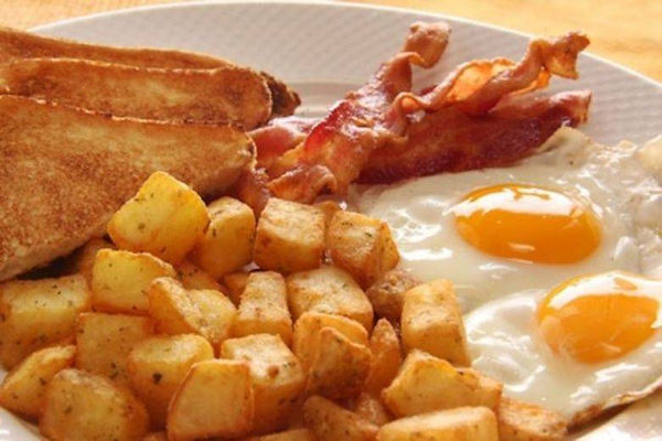Two sunny side up eggs, bread toasted to perfection, strips of bacon, all surrounding home fries.