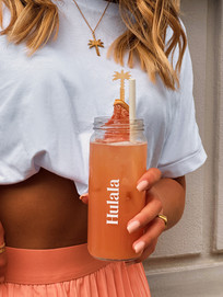 eine braun gebrannte Hulala Mitarbeiterin hält vor sich eine fruchtige Limonade im Hulala Glas.