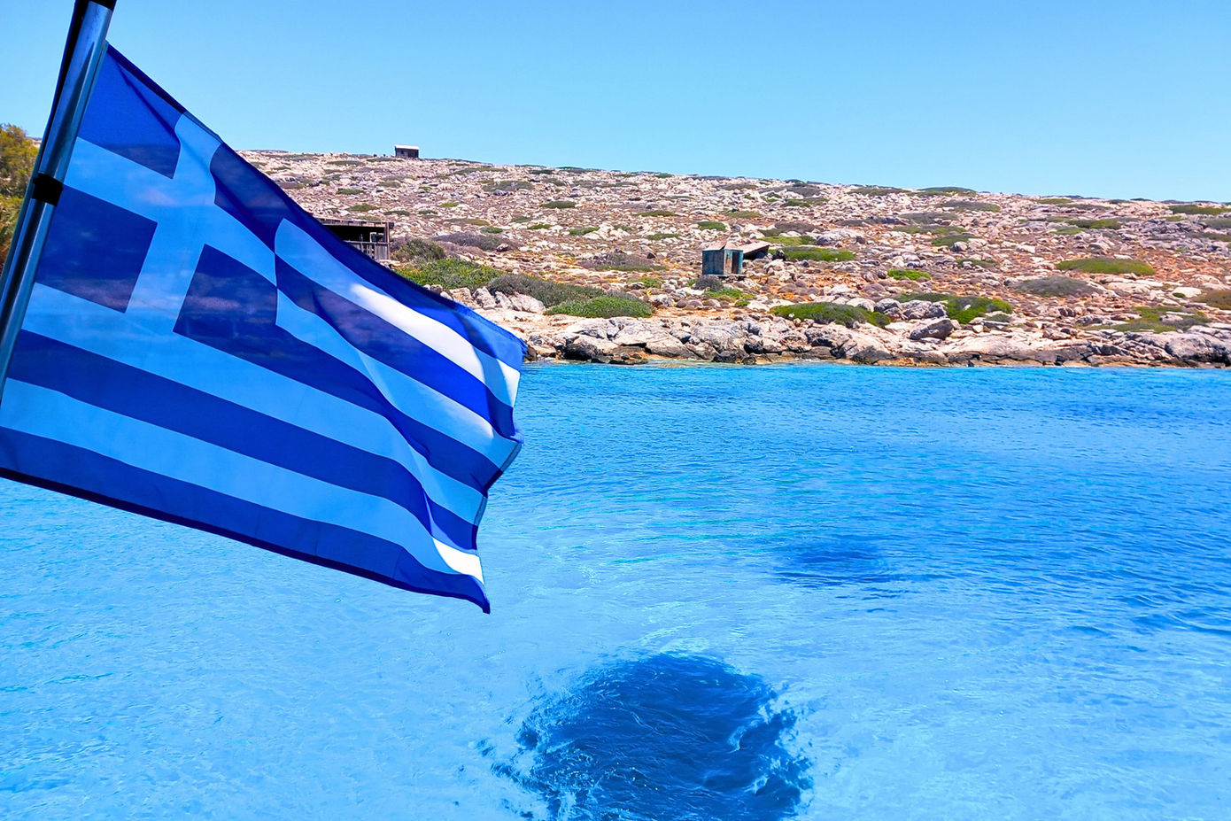 Greek flag on yacht with Dia Island coastline during morning sailing experience in Crete
