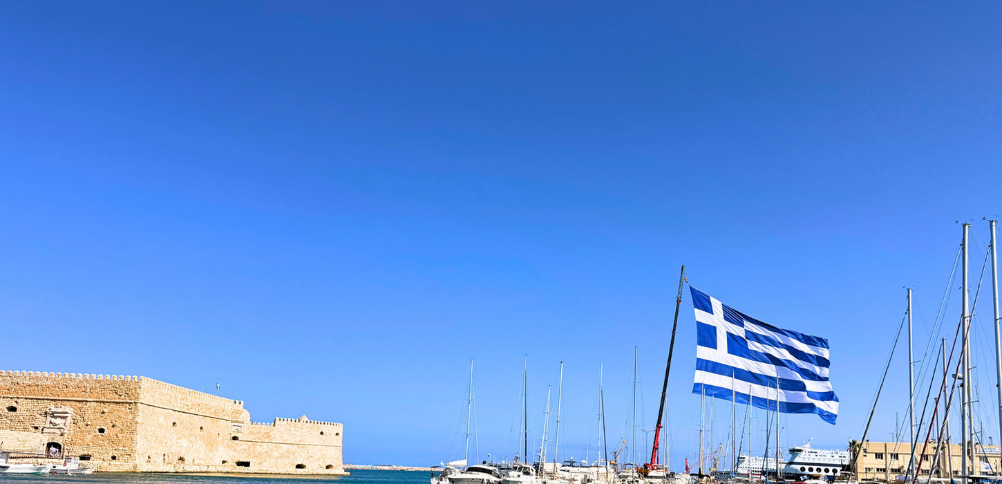 Greek flag at harbor during morning sailing departure to Dia Island in Crete