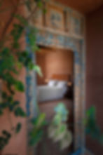Traditional Moroccan bedroom with rustic wooden doors and earthy tones, offering luxurious comfort and cultural charm at the retreat’s accommodations.