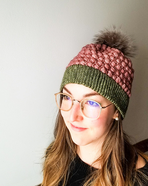 une femme porte des lunettes et une tuque rose et verte avec pompon