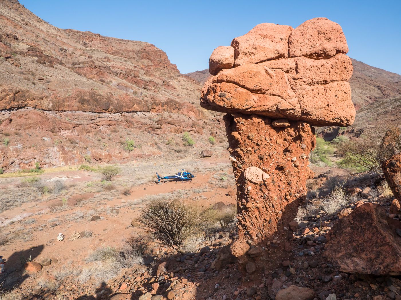 Helicopter on the ground beside a tall red rock pillar