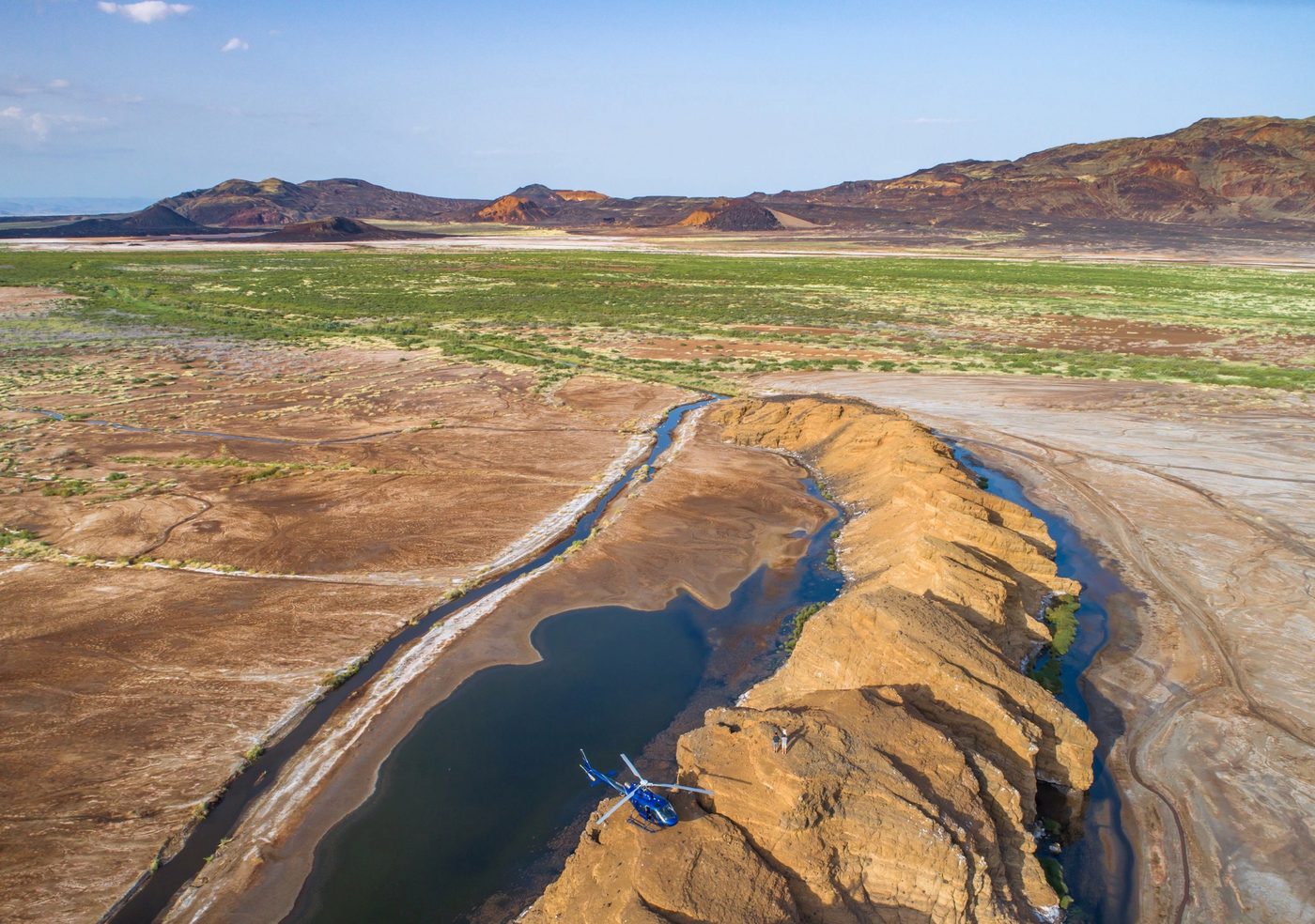 Blue helicopter landed on top of an ochre sandstone ridge between water channels near Lake Turkana, Kenya