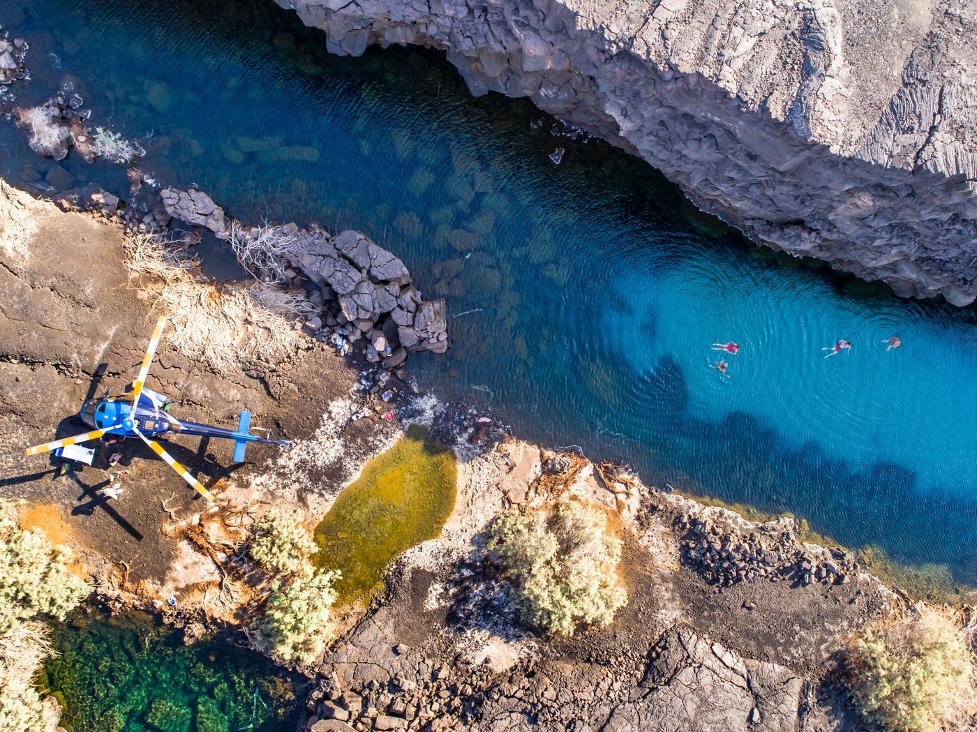 Guests swimming in a clear blue gorge beside the landed helicopter, seen from above