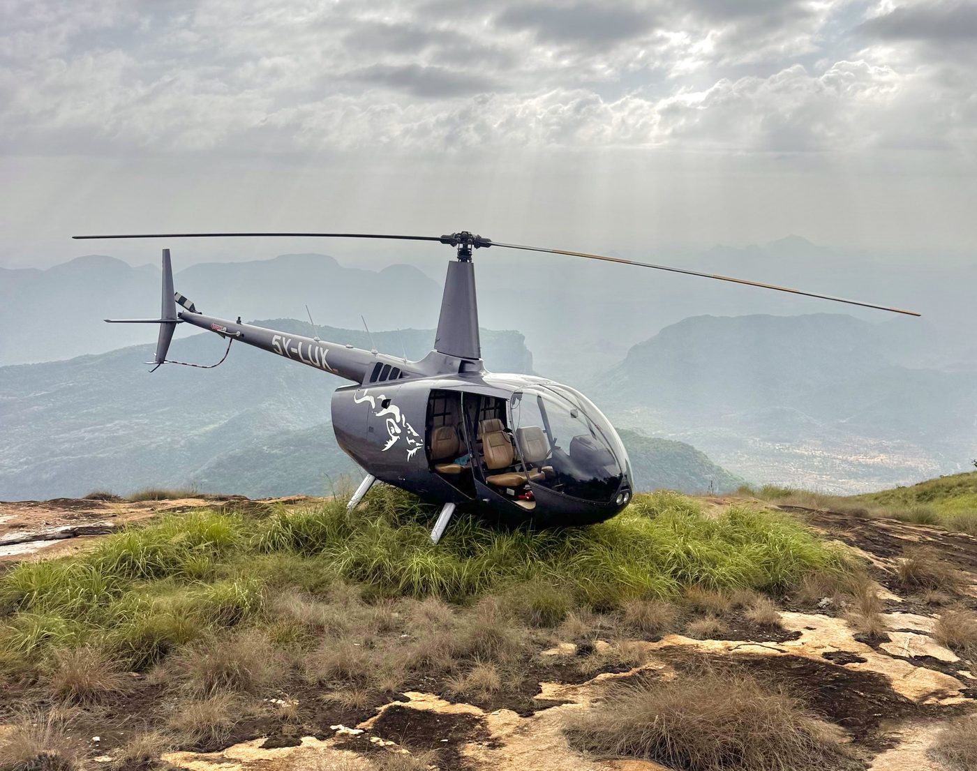 Robinson R66 with its rear doors removed, landed on a grassy mountain top in northern Kenya