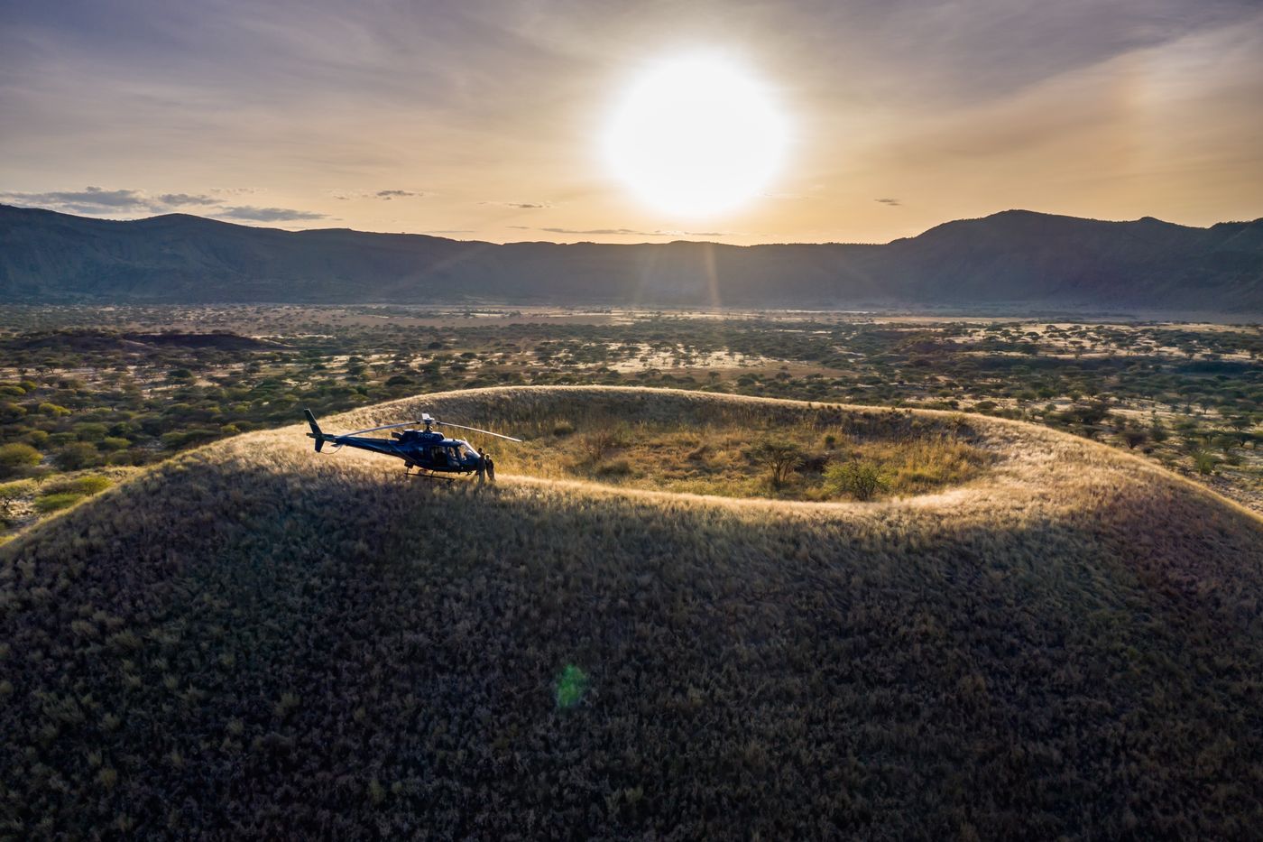 Helicopter landed on the rim of a grassy volcanic crater at sunset, Kenya