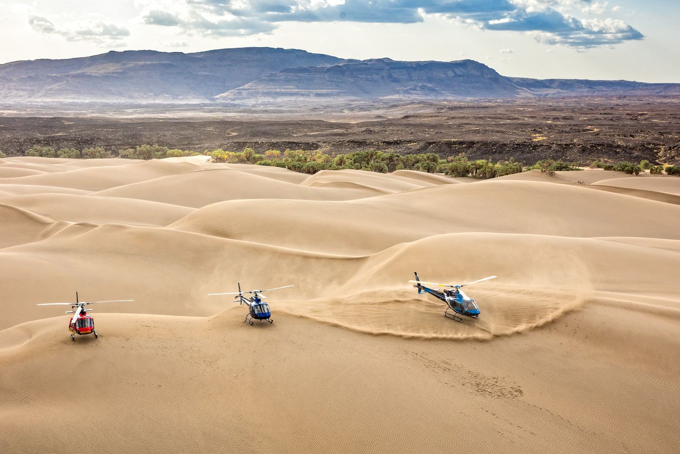 Three helicopters landed in a sea of sand dunes