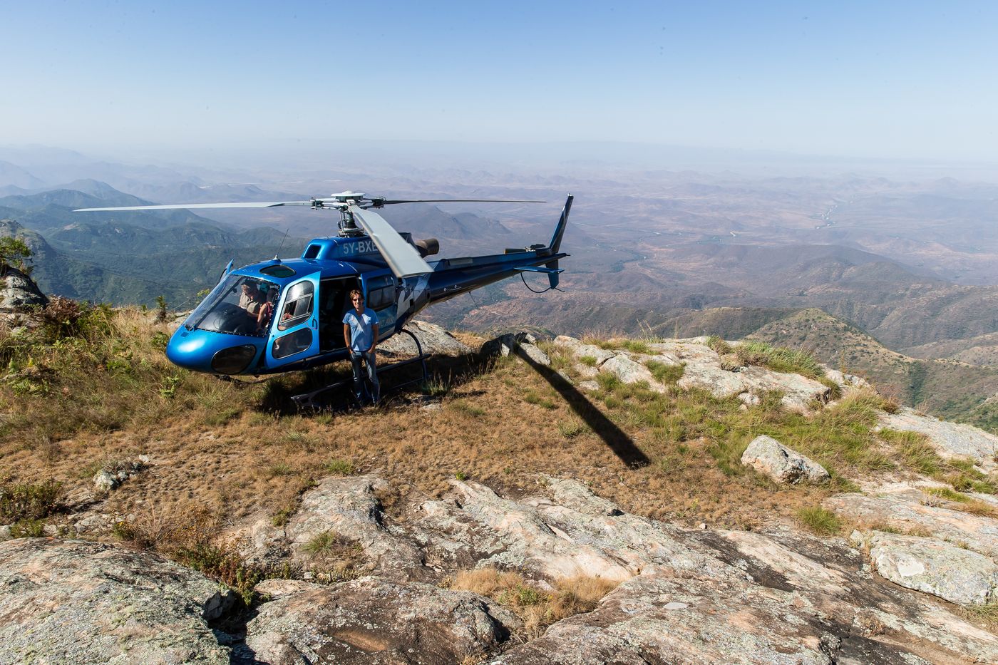 Helicopter parked on a rocky mountain top above a wide valley