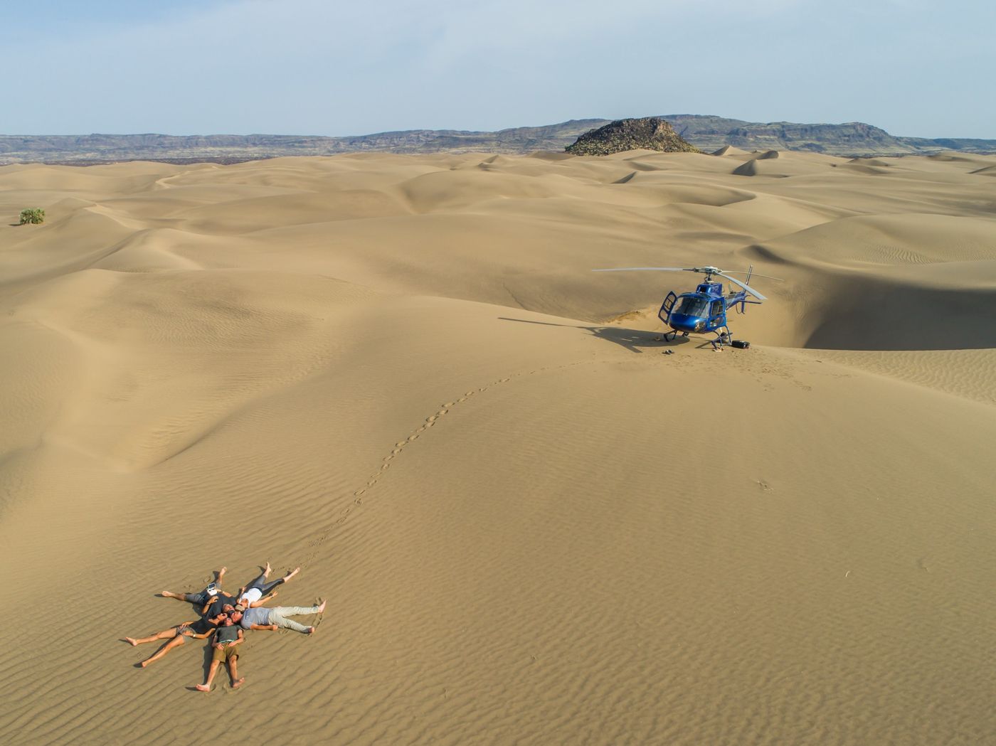 Helicopter on a sand dune with guests lying in the sand
