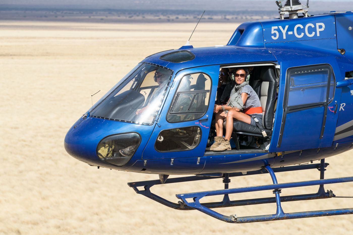 Guest seated at the open sliding door of a helicopter in flight over the savanna