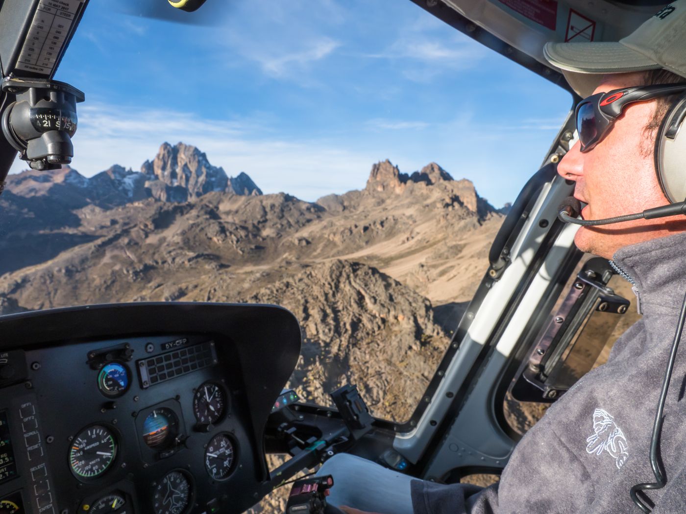 Pilot in the cockpit flying past jagged mountain peaks